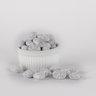 Powdered toffee-coated almonds displayed in a fluted white bowl, with several pieces scattered in front, showcasing their light, powdery coating and irregular texture.