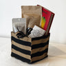 Gift basket from Saratoga Chocolate Co. displayed on a white background, featuring a burlap tote with black stripes containing the book “Wild Chocolate” by Rowan Jacobsen, a 70% dark chocolate bar, strawberry hazelnut bark, and a small bag of cacao nibs.