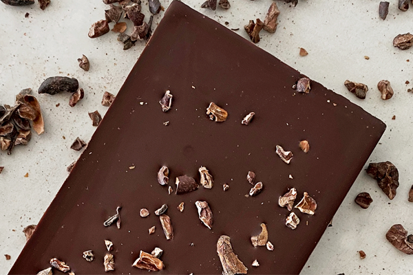 Back side of an uncovered Saratoga Chocolate Co bar, showing a smooth dark chocolate surface sprinkled with cacao beans.