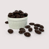 Pile of whole almonds coated in glossy dark chocolate, displayed in a white fluted bowl with several scattered in front.