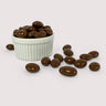 Image shows a pile of milk chocolate coated sea salt almonds displayed in a fluted white bowl with pile of milk chocolate sea salt almonds scattered in front.