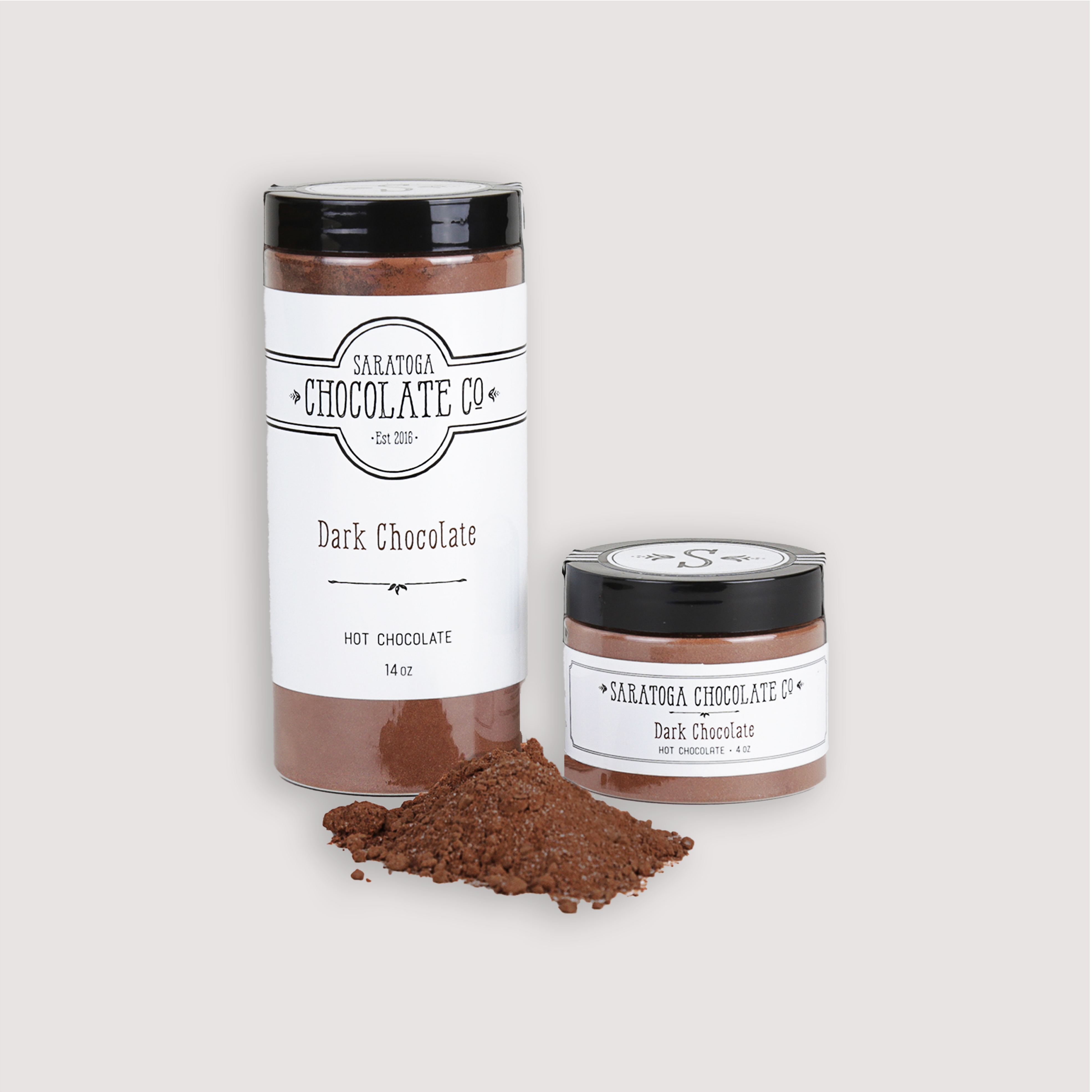Saratoga Chocolate Co. Dark Hot Chocolate Mix displayed in two jar sizes: one 14-ounce jar and one 4-ounce jar, both labeled and sealed. A small pile of rich dark hot chocolate powder is placed in the foreground, showcasing the premium drinking chocolate blend. This product is gluten and dairy free.