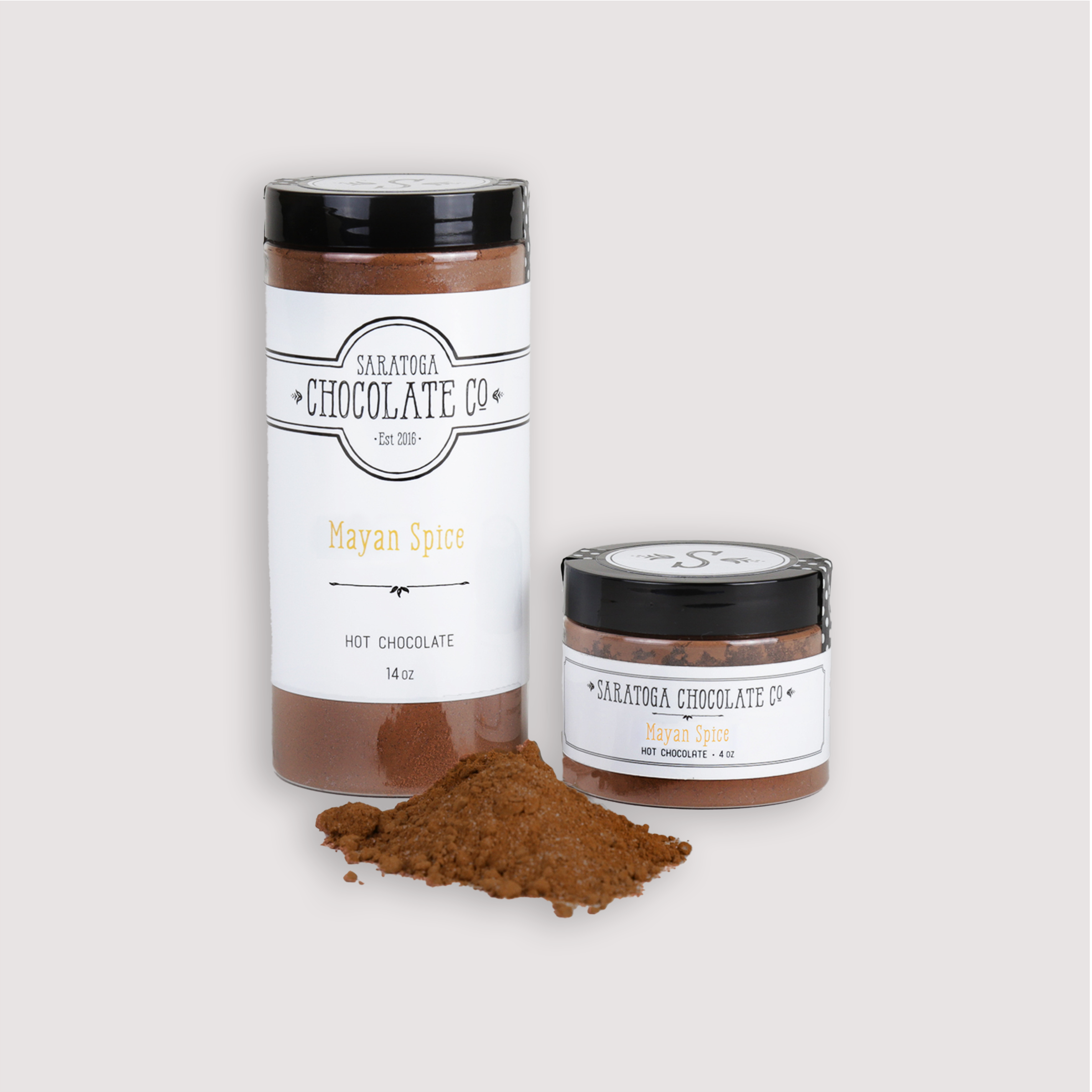 Large & Small Jar with mix in foreground: Saratoga Chocolate Co. Mayan Hot Chocolate Mix displayed in two jar sizes: one 14-ounce jar and one 4-ounce jar, both labeled and sealed. A small pile of rich Mayan spice hot chocolate powder is placed in the foreground, showcasing the premium drinking chocolate blend. This product is gluten and dairy free.