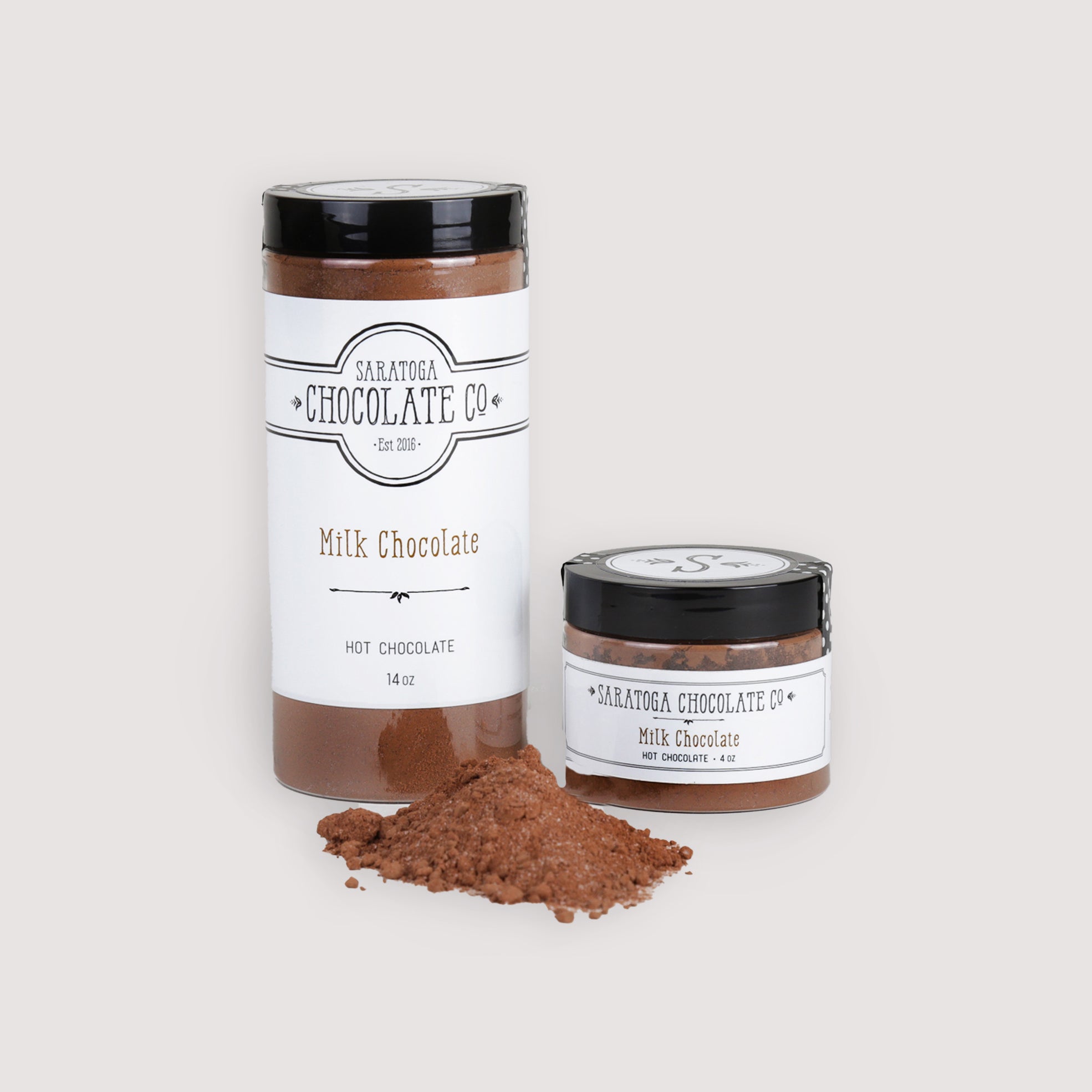 Large & Small Jar with mix in foreground: Saratoga Chocolate Co. Milk Hot Chocolate Mix displayed in two jar sizes: one 14-ounce jar and one 4-ounce jar, both labeled and sealed. A small pile of rich Milk hot chocolate powder is placed in the foreground, showcasing the premium drinking chocolate blend. This product is gluten free.