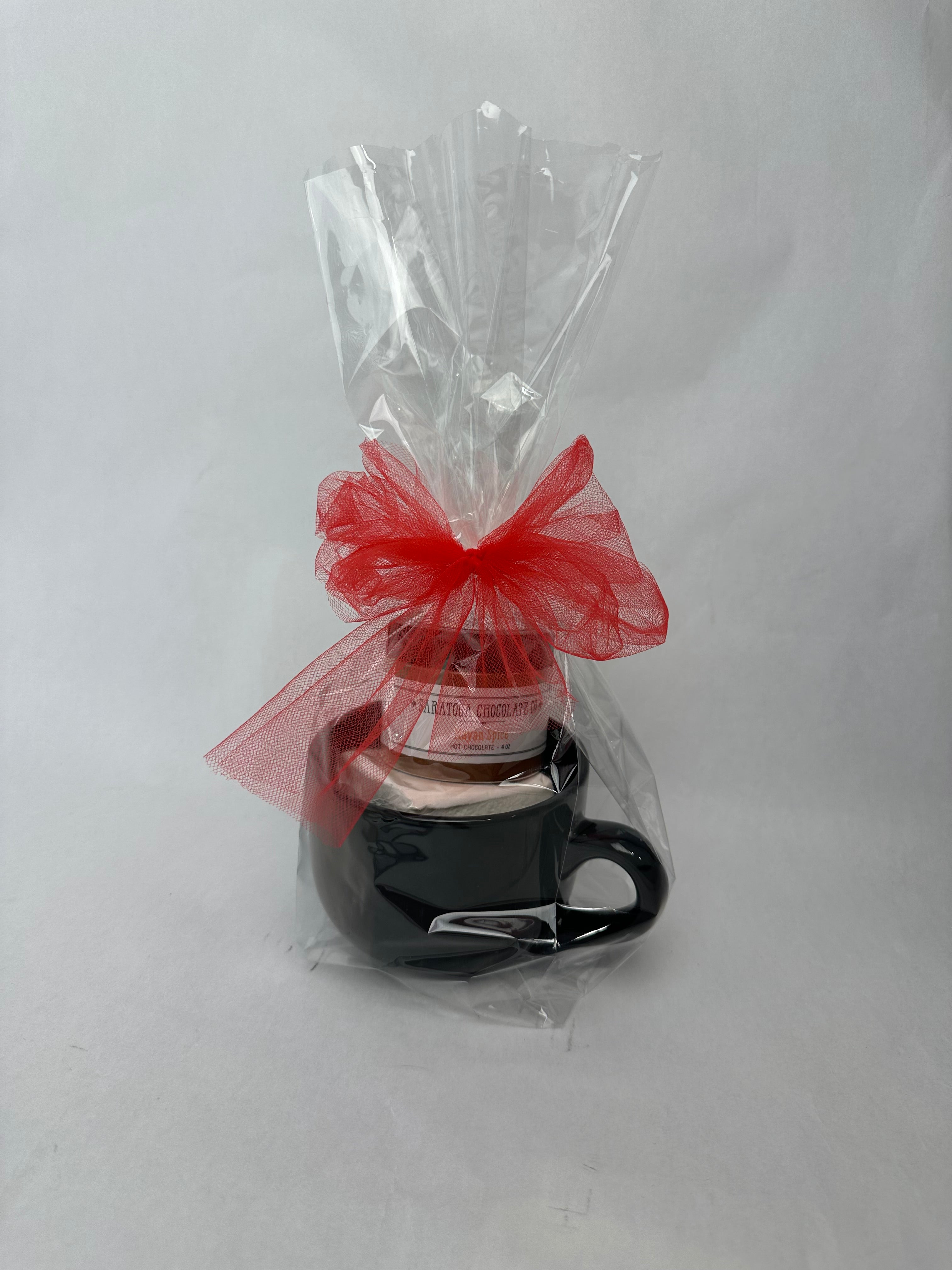 Black ceramic mug hot chocolate gift set wrapped in clear cellophane with a red bow, containing Saratoga Chocolate Co. Maya Spice drinking chocolate and a jumbo vanilla marshmallow