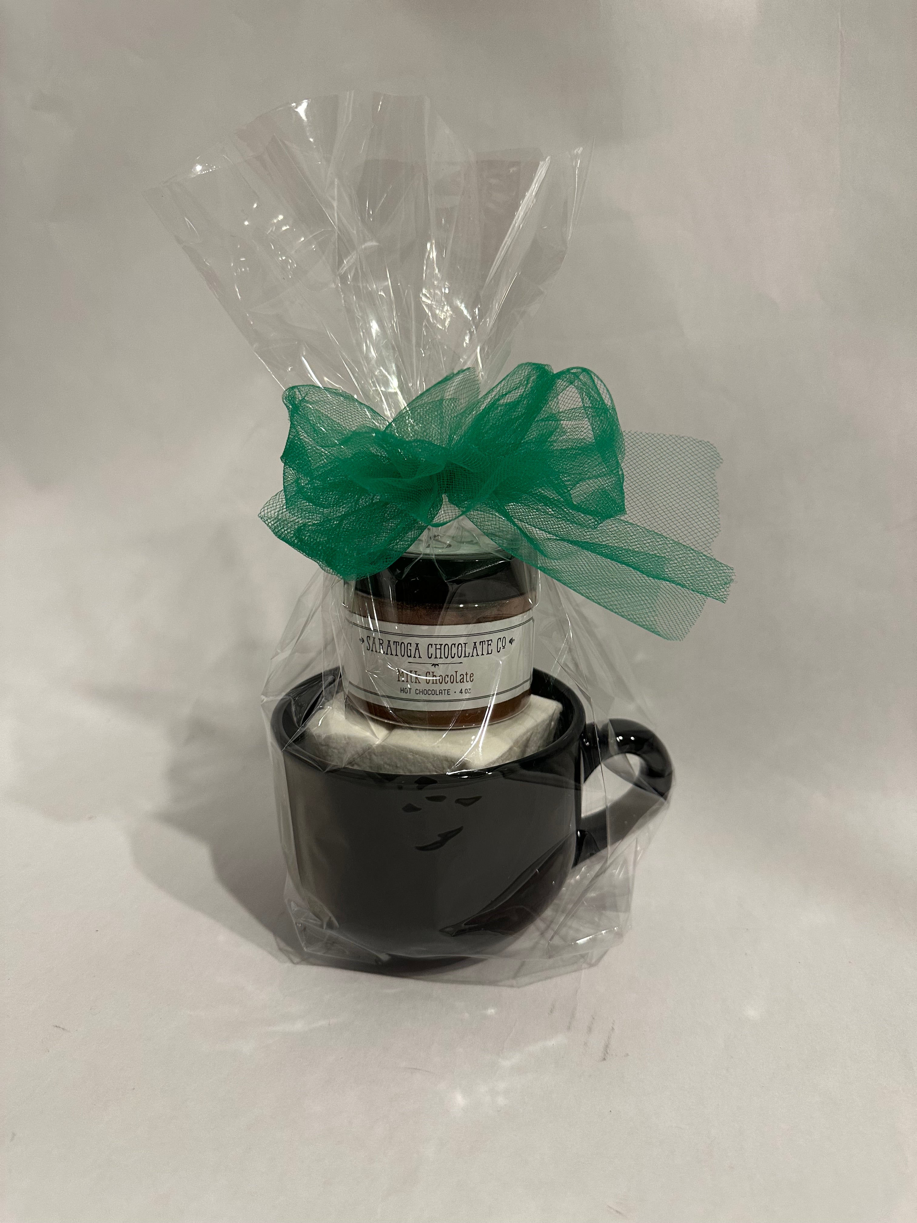 Black ceramic mug hot chocolate gift set wrapped in clear cellophane with a green bow, containing Saratoga Chocolate Co. Milk Chocolate drinking chocolate and a jumbo vanilla marshmallow.