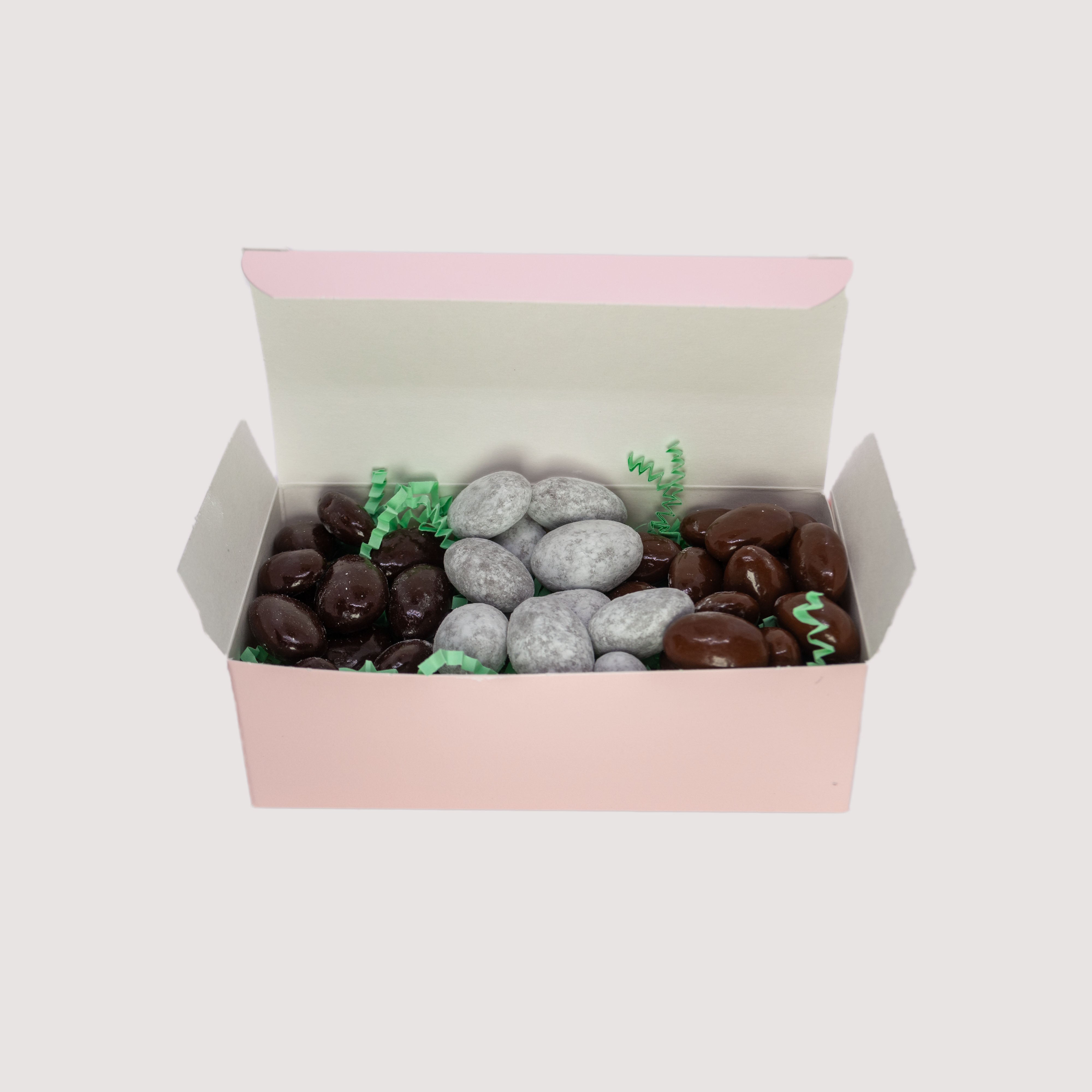 Almond sampler by Saratoga Chocolate Co featuring three types of almonds coated in different kinds of chocolate, arranged in separate sections within a pink rectangular box.