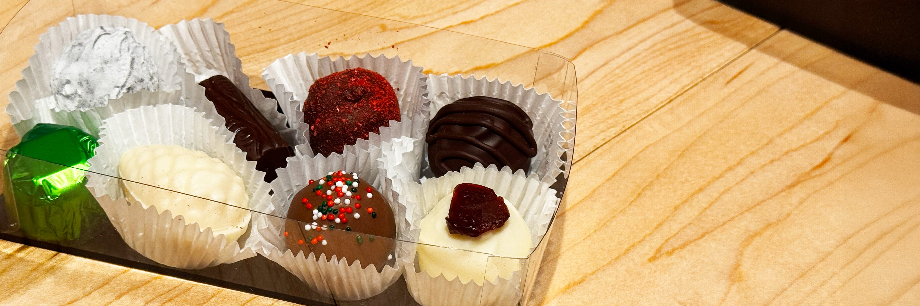 Assorted chocolate truffles in white paper wrappers on a wooden surface