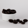 Image shows a pile of dark chocolate brandied cherries displayed in a fluted white bowl with some chocolate covered brandied cherries scattered in front of the bowl.