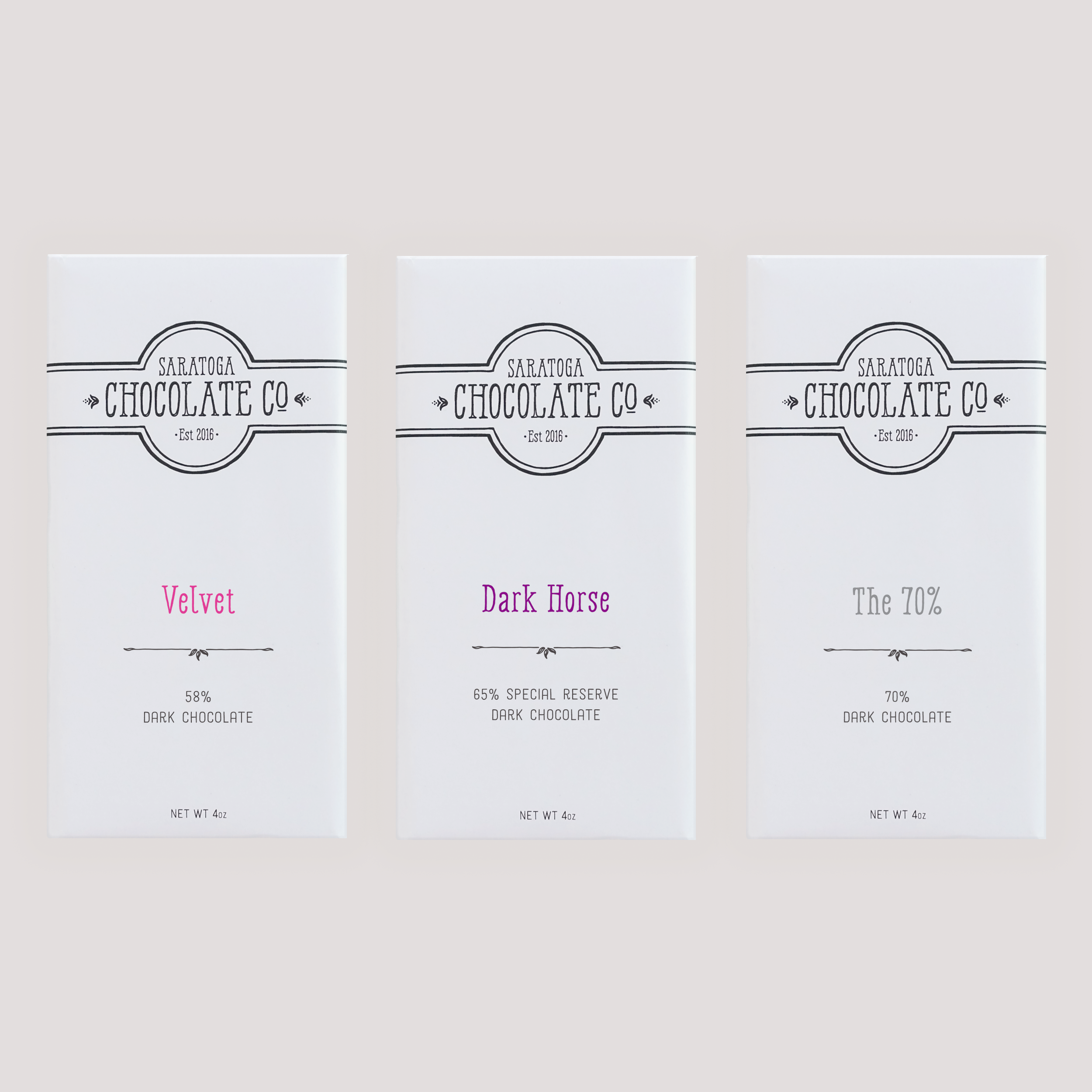 Three Saratoga Chocolate Co. dark chocolate bars in white wrappers with labels: Velvet, Dark Horse and 70%; displayed side by side on a neutral background.
