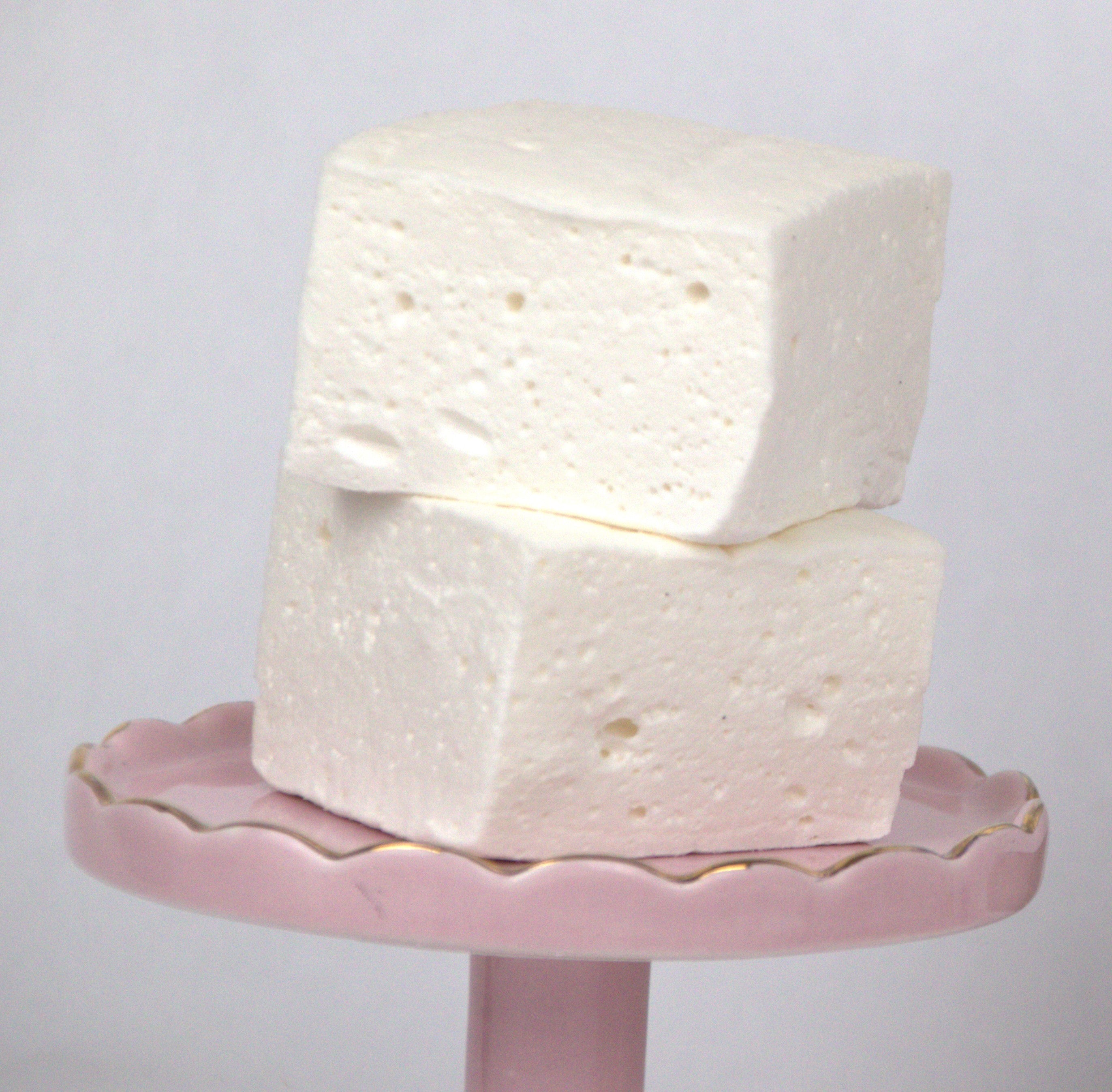 ​Individually wrapped Saratoga Chocolate Co. Jumbo Vanilla Marshmallow in clear cellophane packaging with an adhesive closure and label. The marshmallow appears pillow-soft, square-shaped, and dusted with a light coating of powdered sugar and cornstarch.