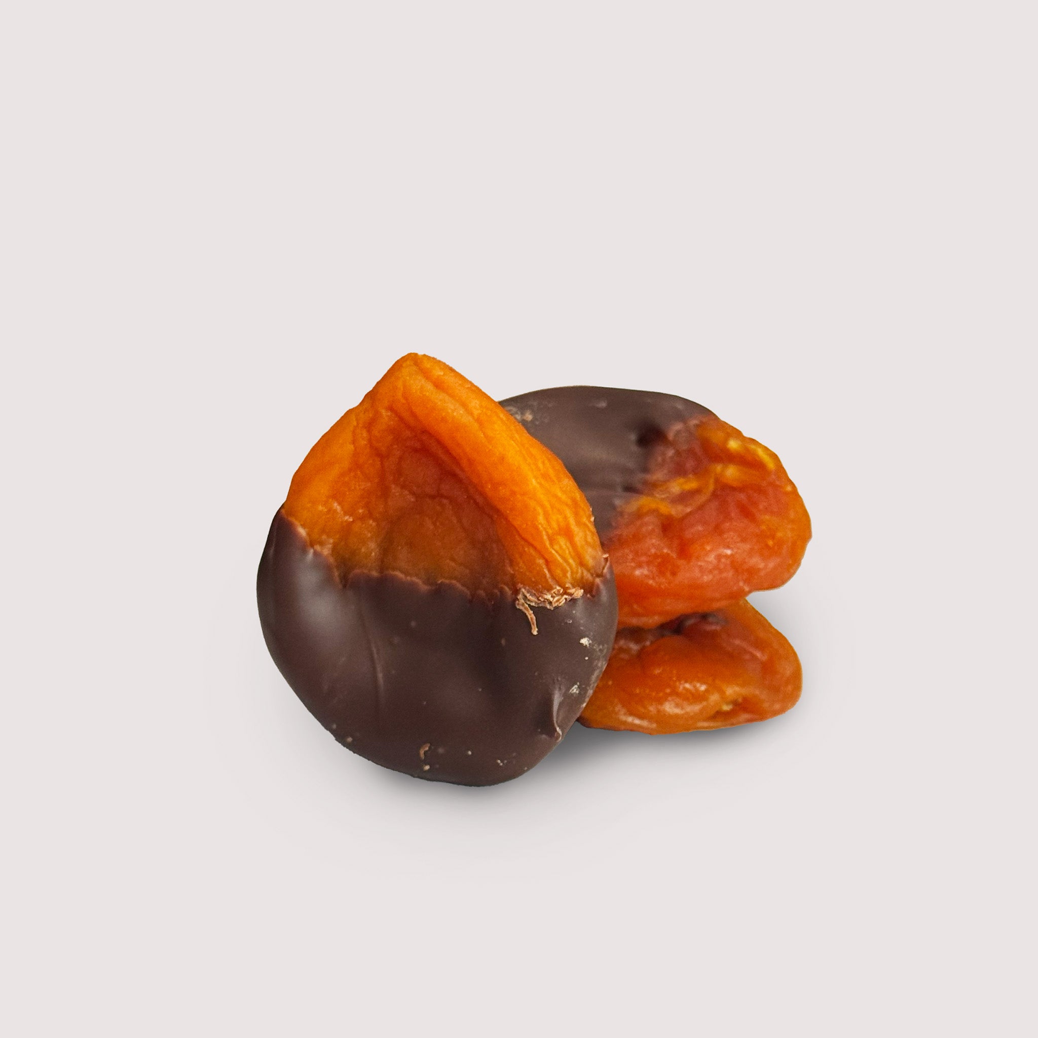 Apricots dipped in dark chocolate by Saratoga Chocolate Co on a neutral background