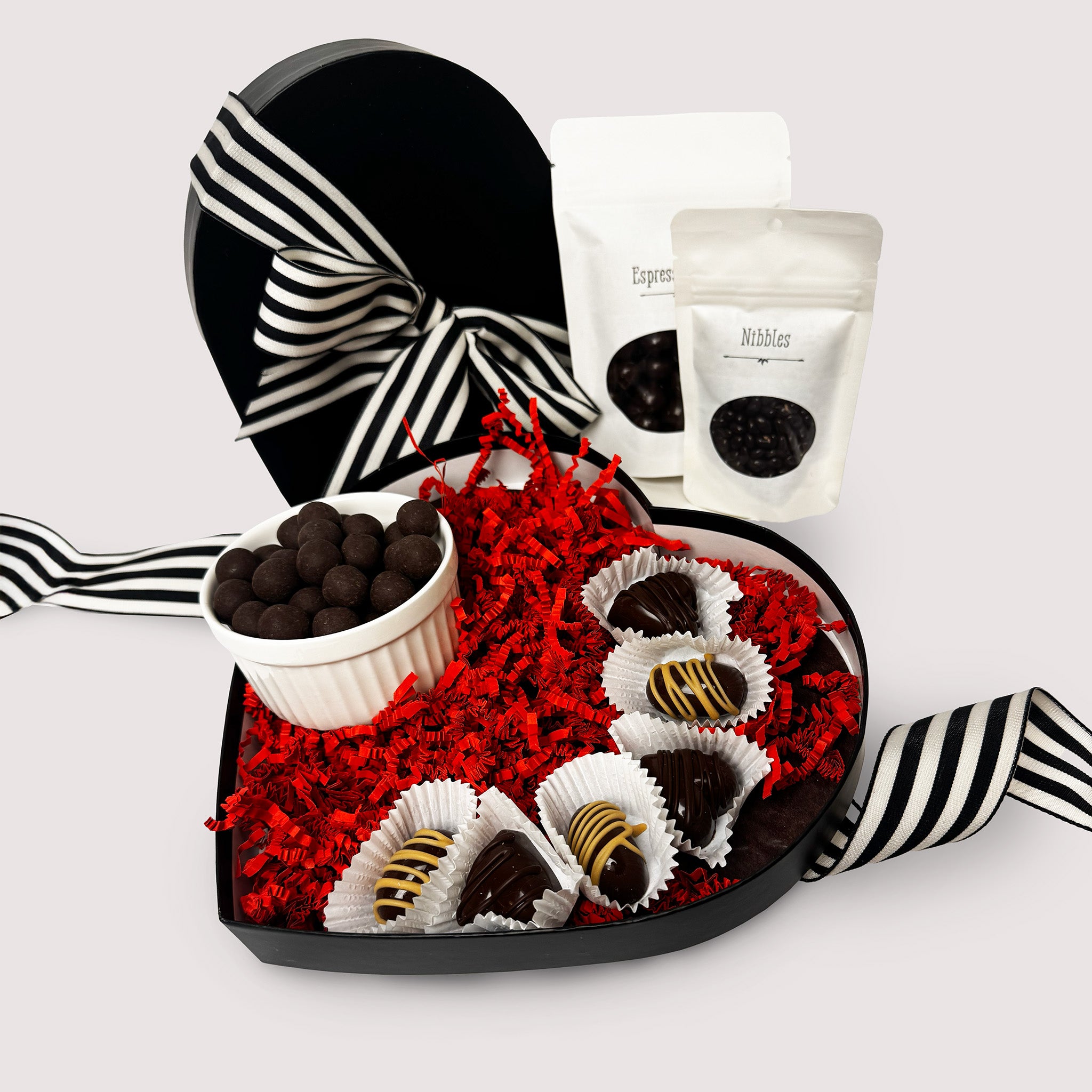 Heart-shaped black gift box with dark bourbon caramels, chocolate covered espresso beans and nibbles and truffles on a neutral background