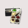 8 assorted colorful truffles in a white paper cups in a open clear box and a sealed box of truffles behind. All displayed in  a neutral background