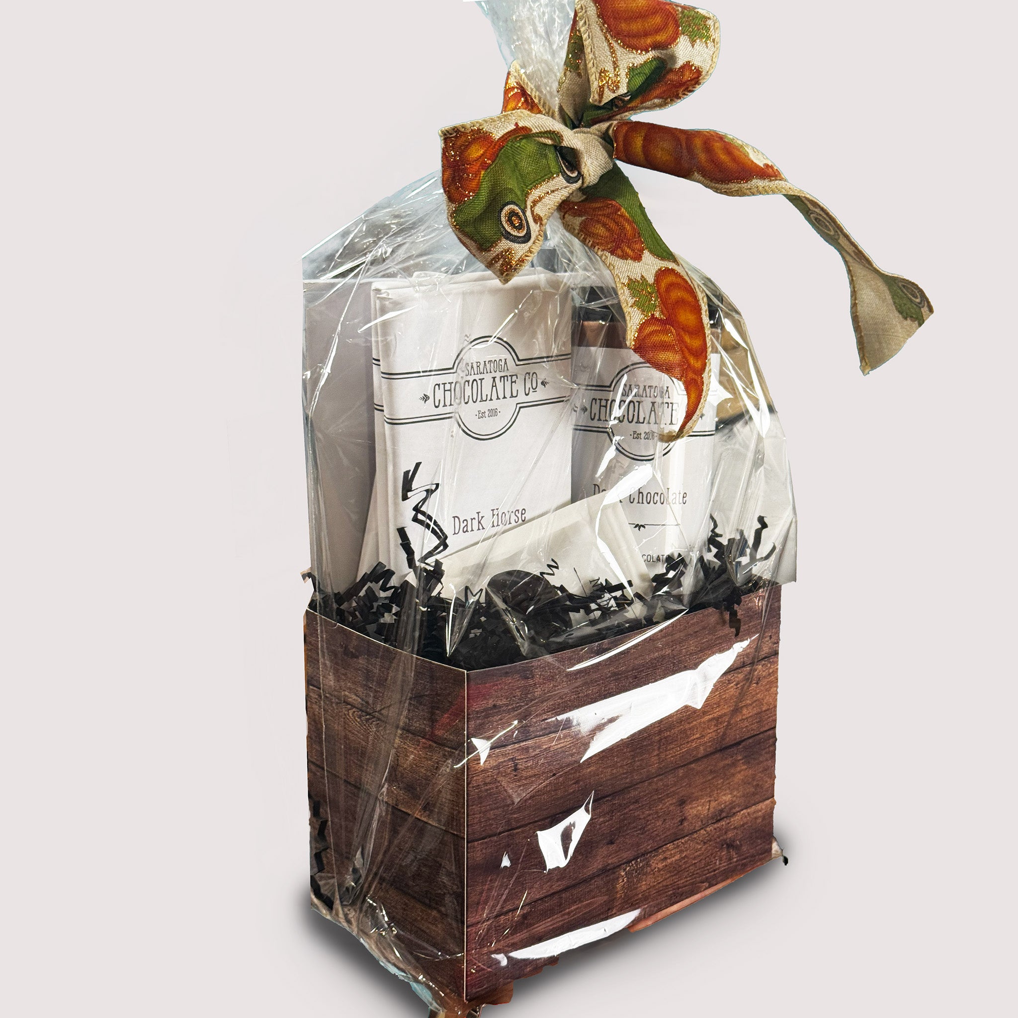 Favorites Gift Basket by Saratoga Chocolate Co with assorted chocolate bars, hot chocolate, and small treats wrapped in clear cellophane with a ribbon.