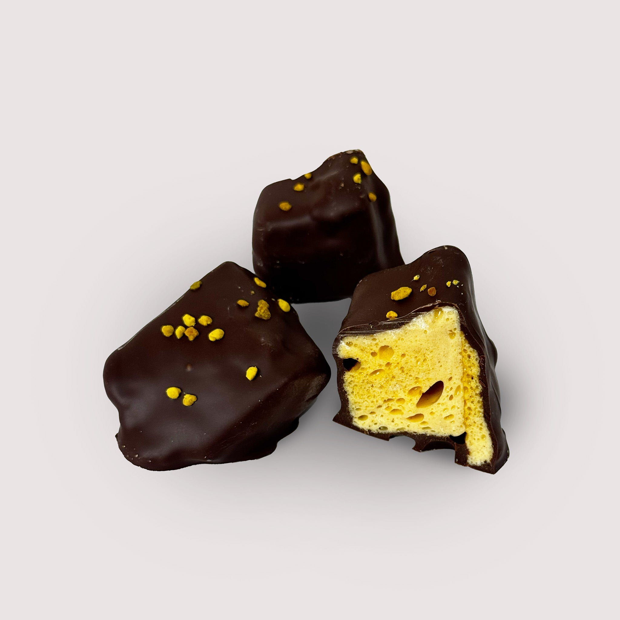 Chocolate-covered honeycomb with bee pollen granules on a light gray background