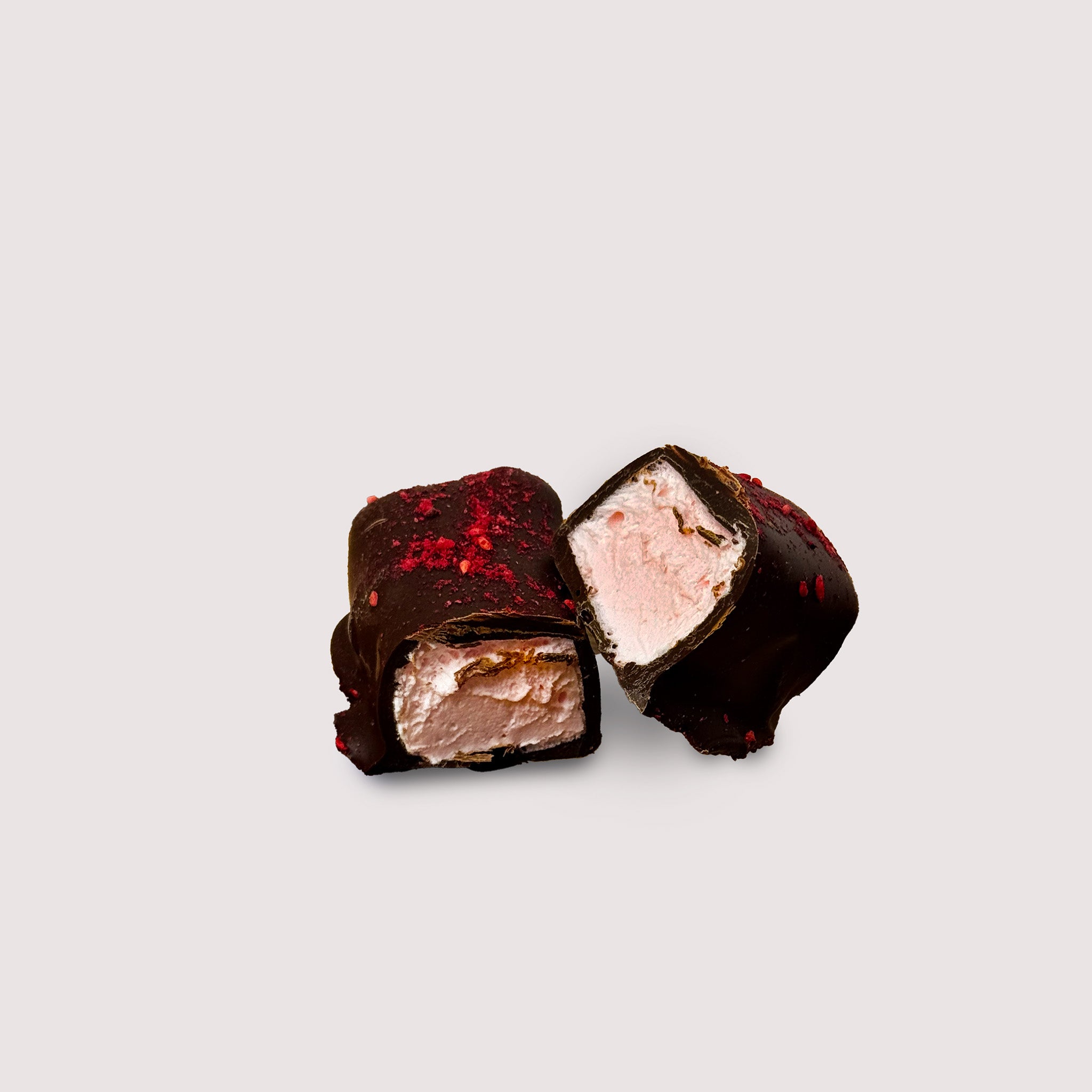 Chocolate-covered raspberry marshmallow with raspberry topping cut in halves on a light gray background