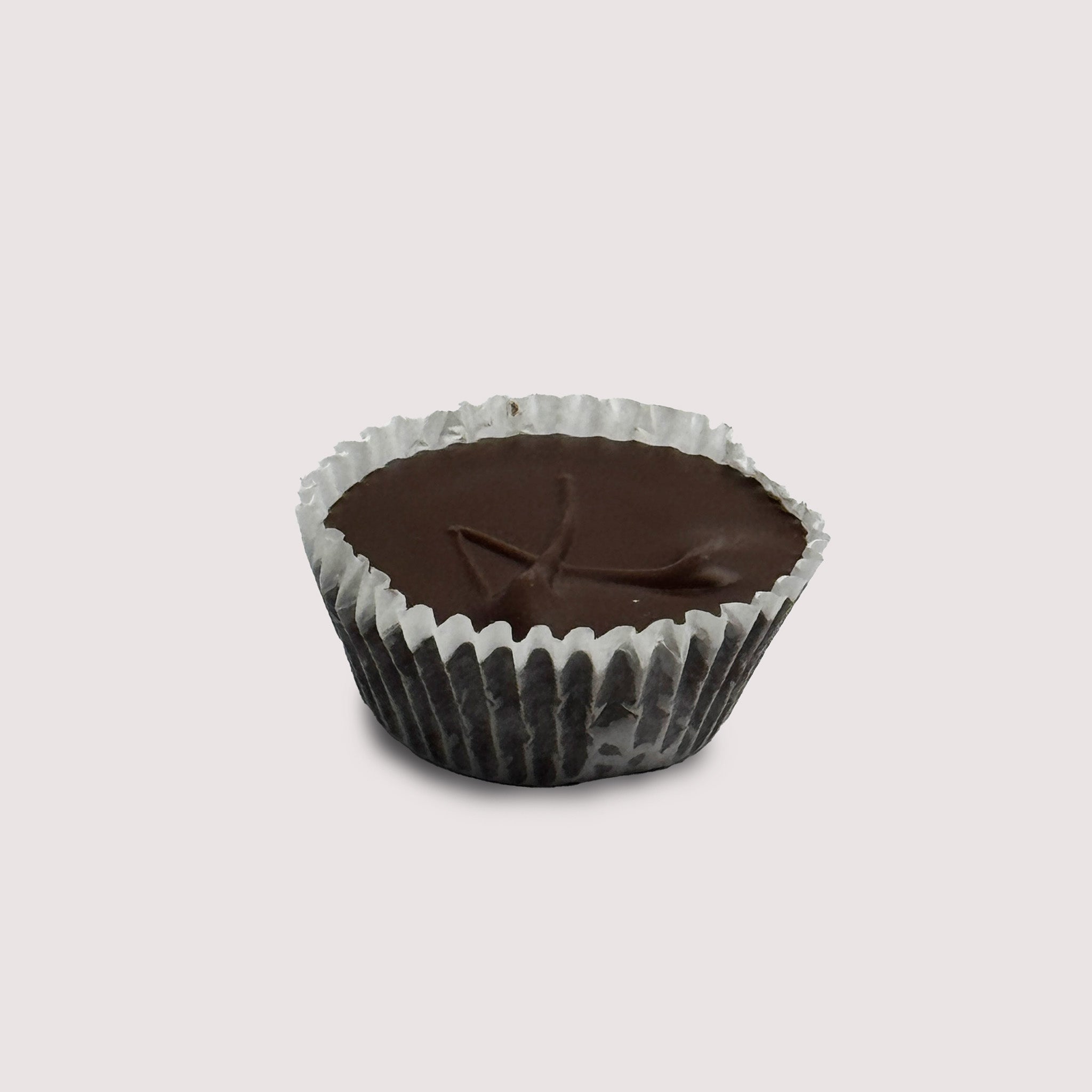 One Milk Chocolate Peanut Butter Cup placed in a white paper cup, sitting on a light, neutral background. The chocolate has a smooth, glossy top and is presented simply to highlight its rich texture.