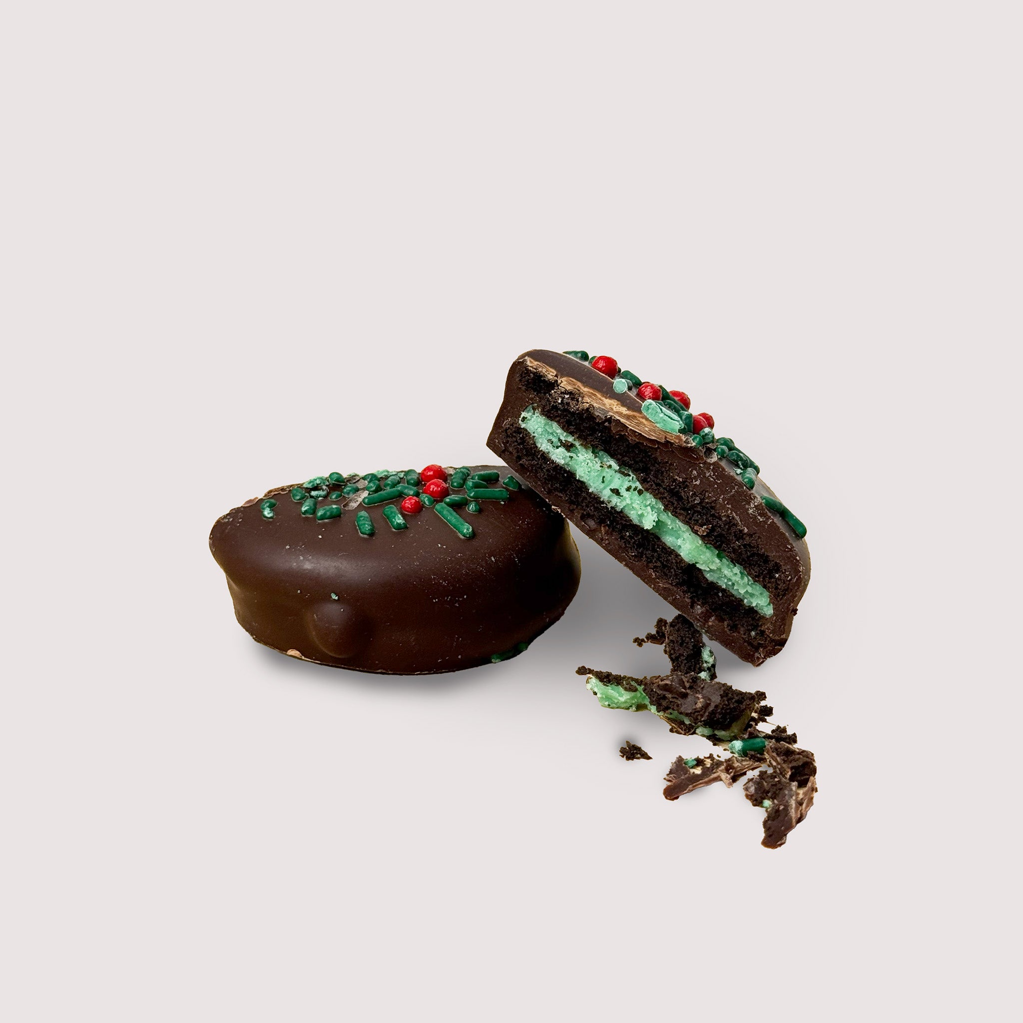 Mint Oreo dipper in dark chocolate cut in half with green and red topping, all displayed on a light background