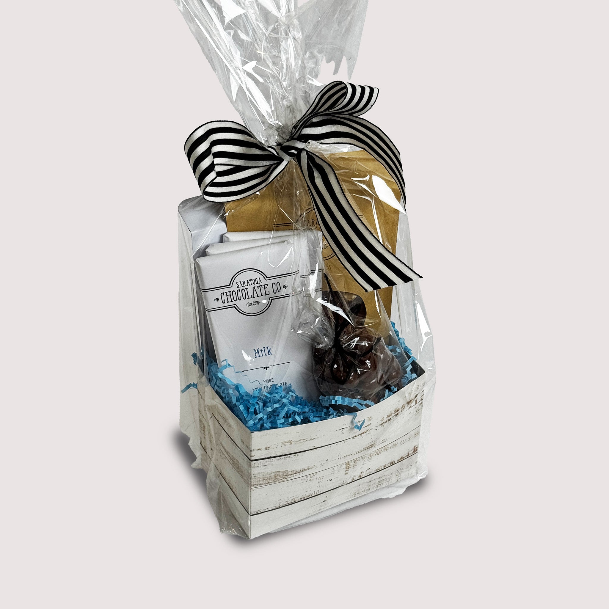 Gift basket from Saratoga Chocolate Co. containing a Milk Chocolate, Bodhi & Toasted Sesame Bar, a bag of milk chocolate–covered almonds, and a bag of Strawberry Hazelnut Bark, wrapped in a clear bag with a black-and-white striped ribbon.