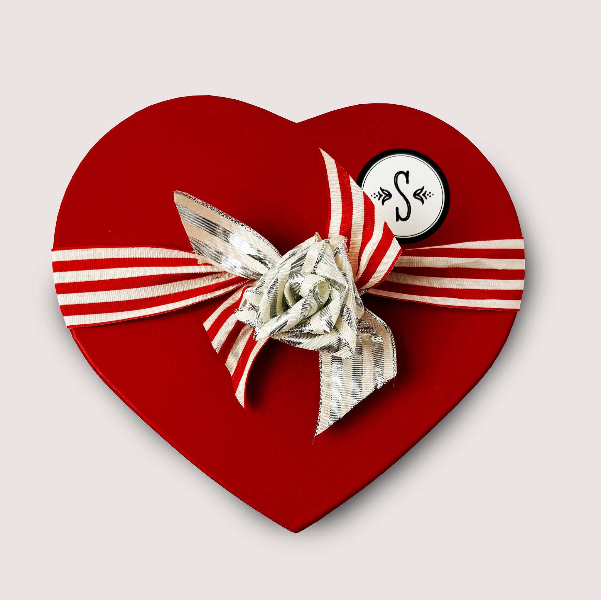 Heart-shaped red box with a silver bow and Saratoga Chocolate logo on a light gray background