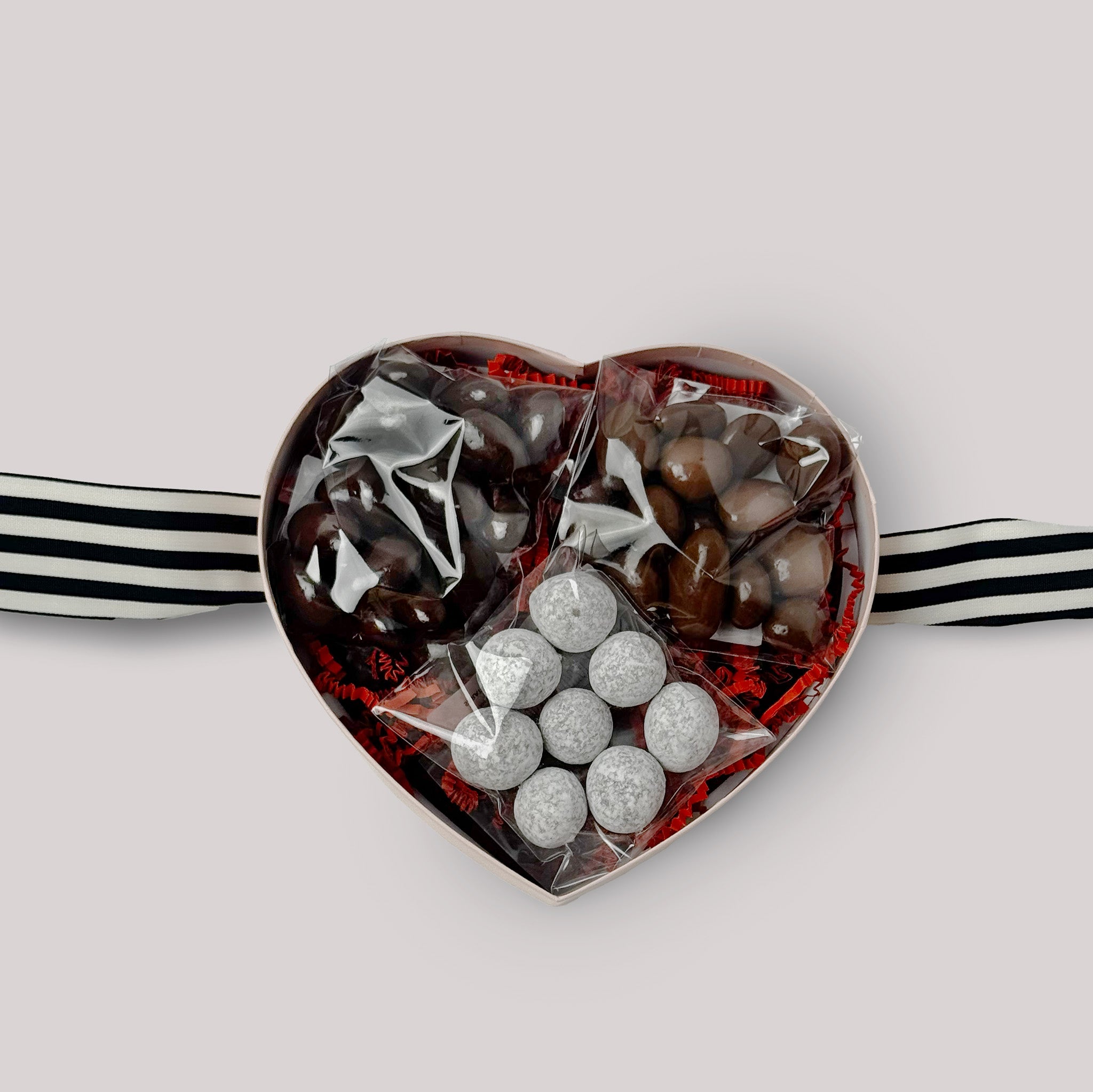 Open heart-shaped box of chocolates with toffee, dark and milk chocolate covered nuts on a neutral background