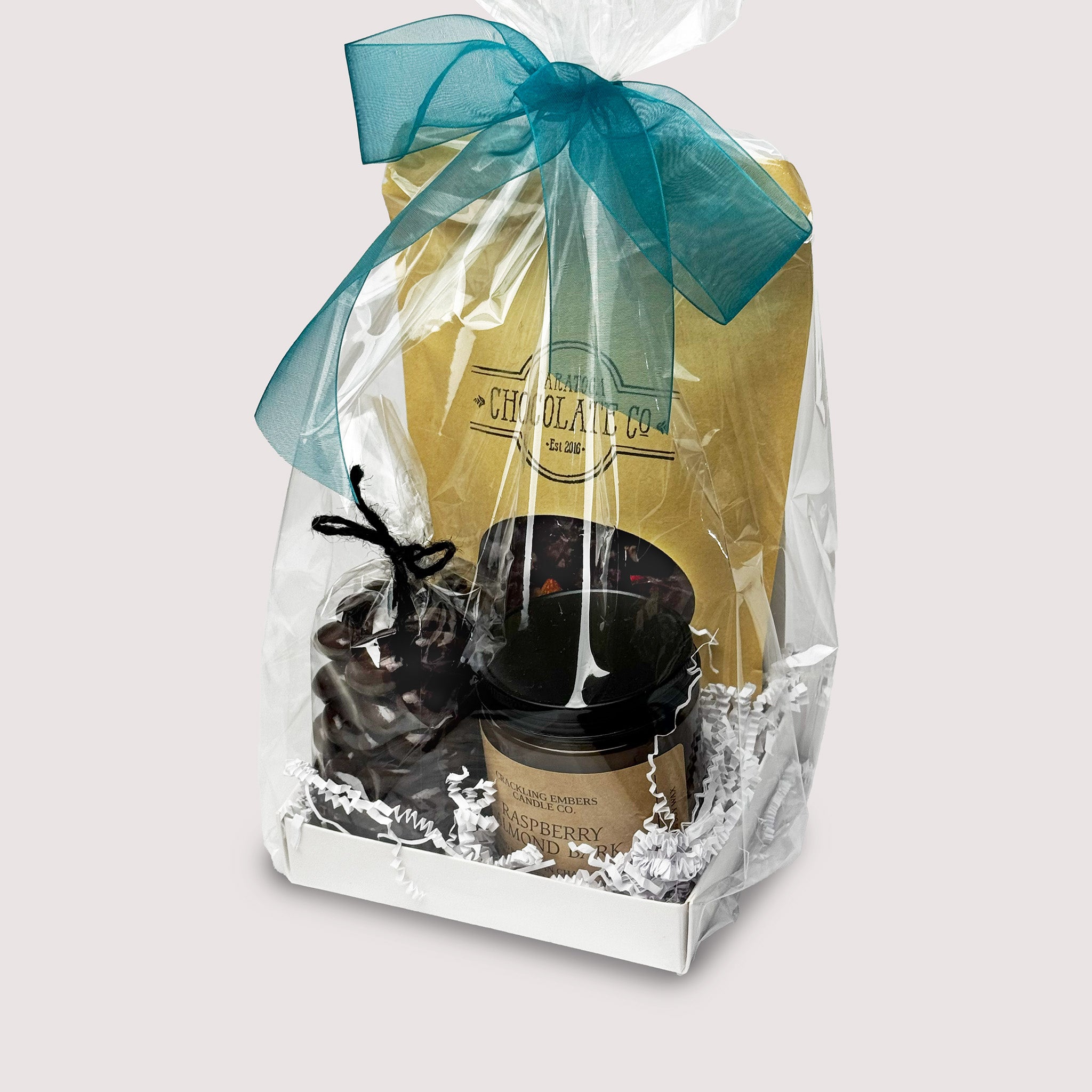 Gift set with a bag of chocolate almonds, a candle, and a bag of chocolate bark on a neutral background