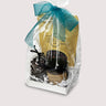 Gift set with a bag of chocolate almonds, a candle, and a bag of chocolate bark on a neutral background
