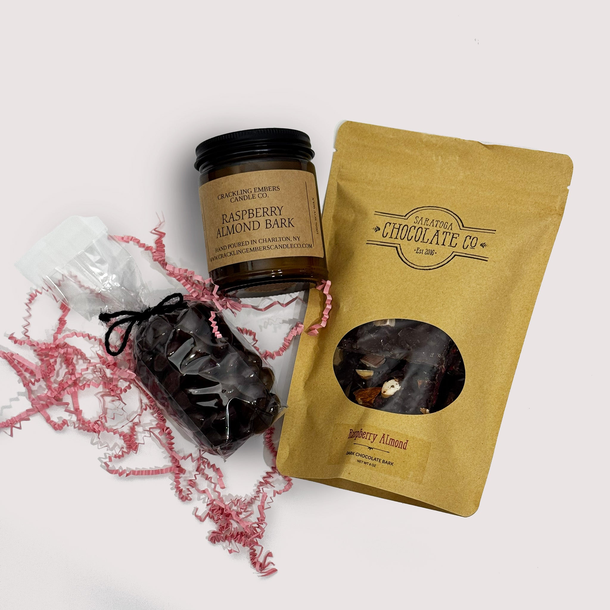 Raspberry Almond bark, bag of chocolate covered almonds with packaging and a candle on a neutral background