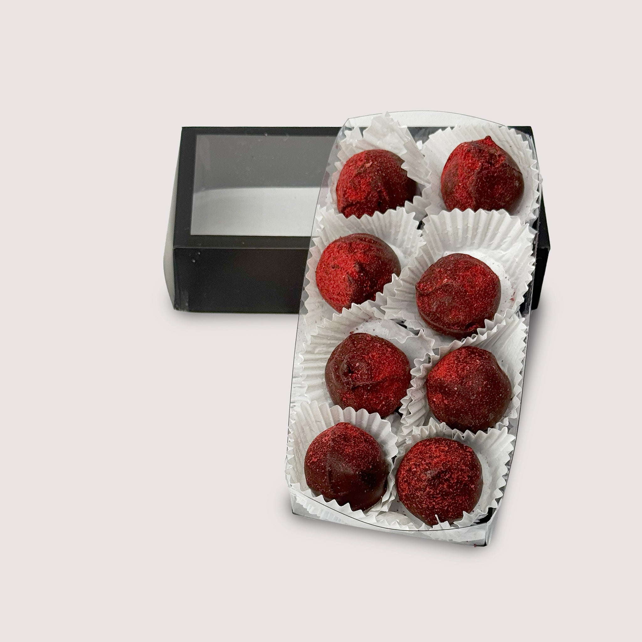 Saratoga Chocolate Co. Raspberry Truffle Collection featuring eight dark chocolate truffles nestled in white paper cups within a clear box. Each truffle has a smooth dark chocolate shell dusted with vibrant red raspberry powder.