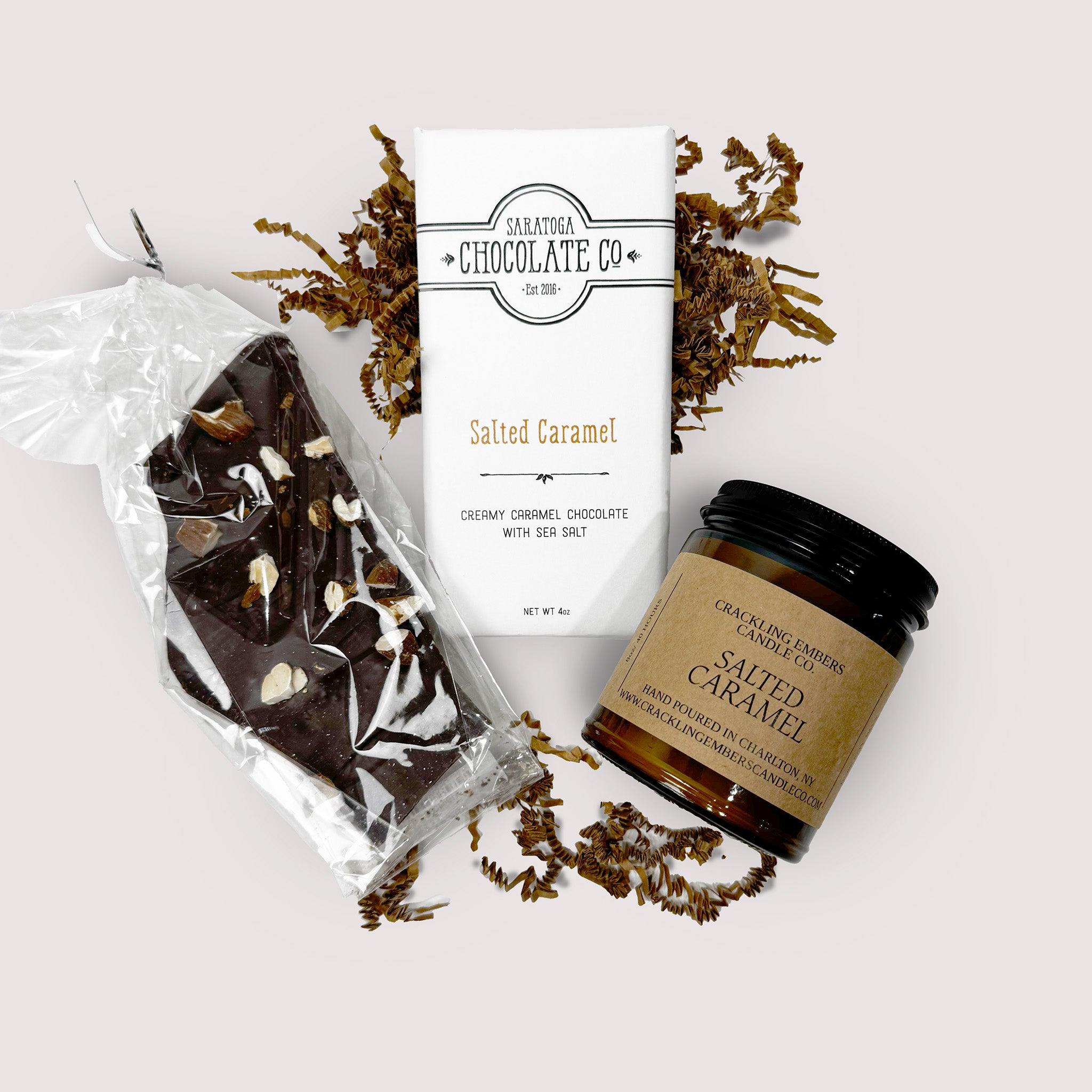 Salted caramel chocolate bar, bark and a candle with packaging from Saratoga Chocolate Co on a white background.