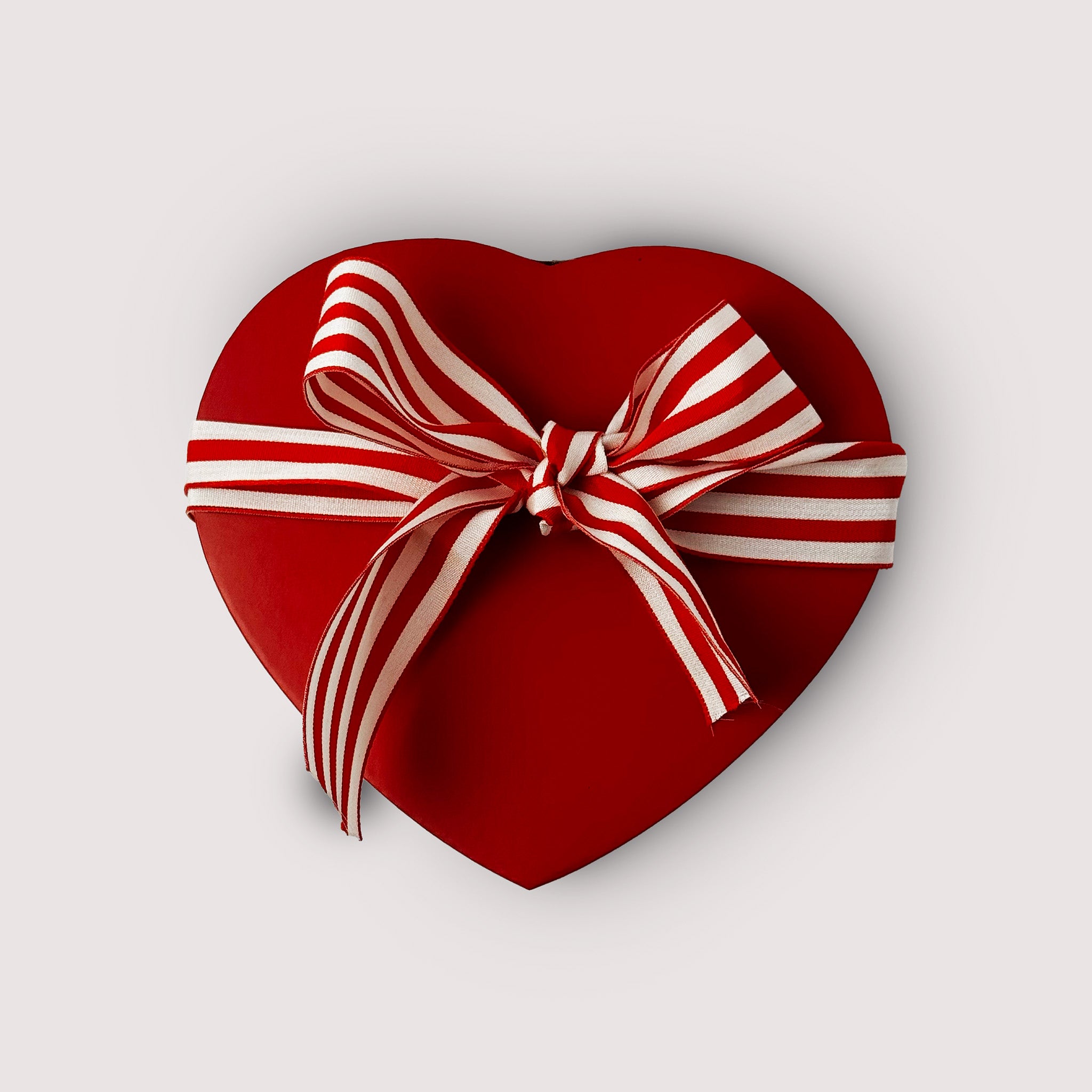 Heart-shaped red gift box with a white and red striped ribbon on a light gray background
