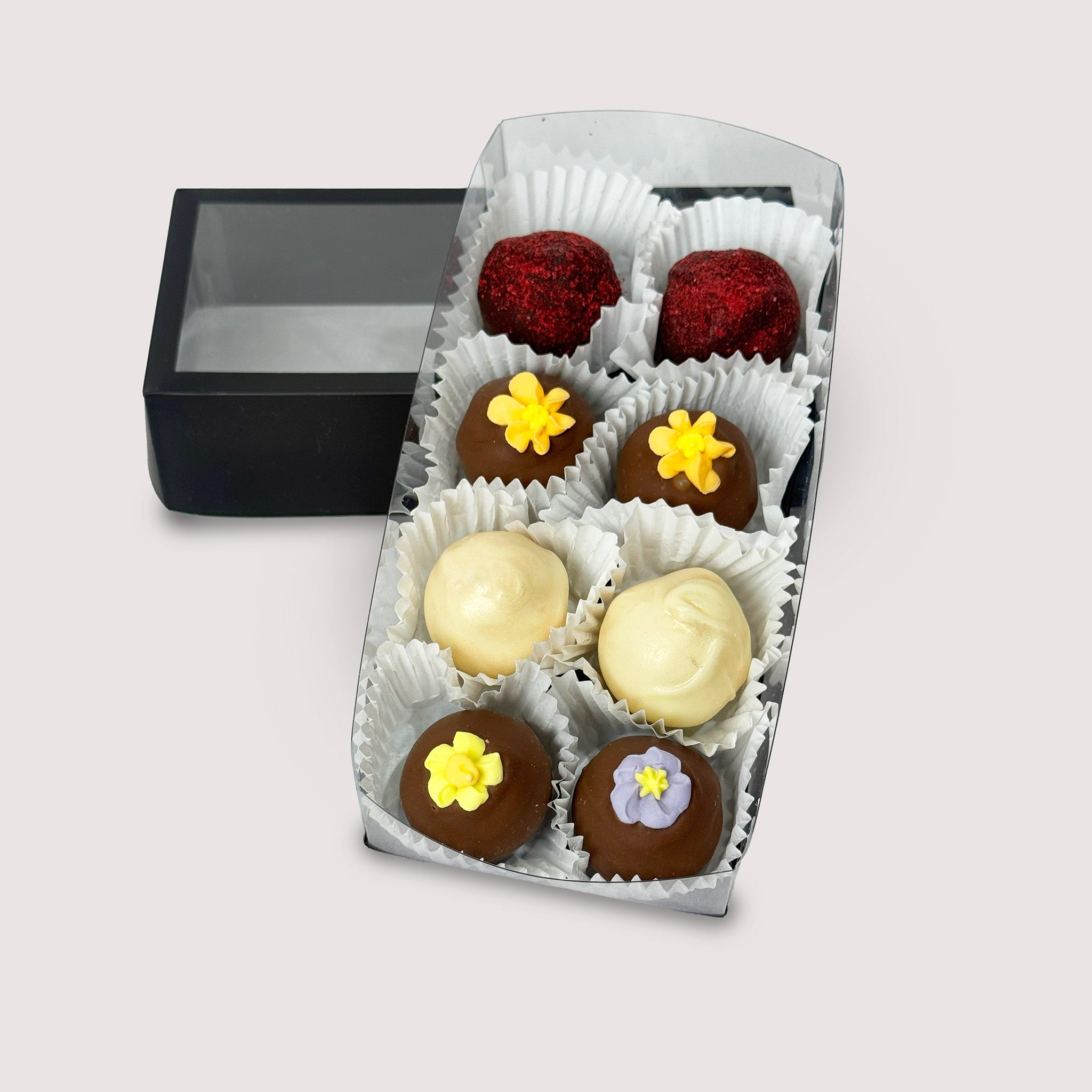 A variety of beautifully decorated truffles in an open box on a neutral background