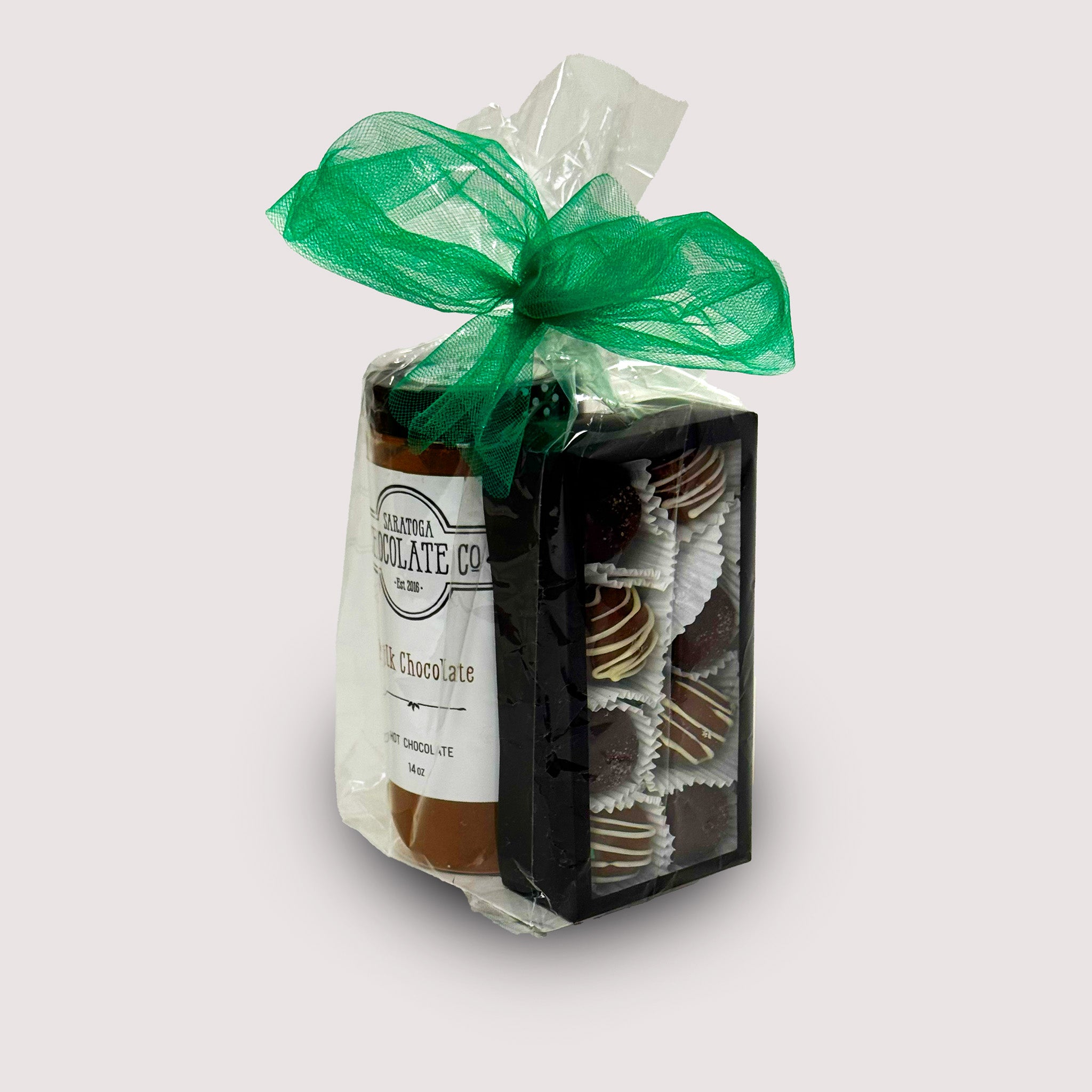 A large Saratoga Chocolate Co. St. Patrick’s Day chocolate bundle includes two handmade Irish Cream and two Irish Coffee truffles paired with a small jar of milk chocolate hot chocolate mix  In a clear bag with green ribbon on top.