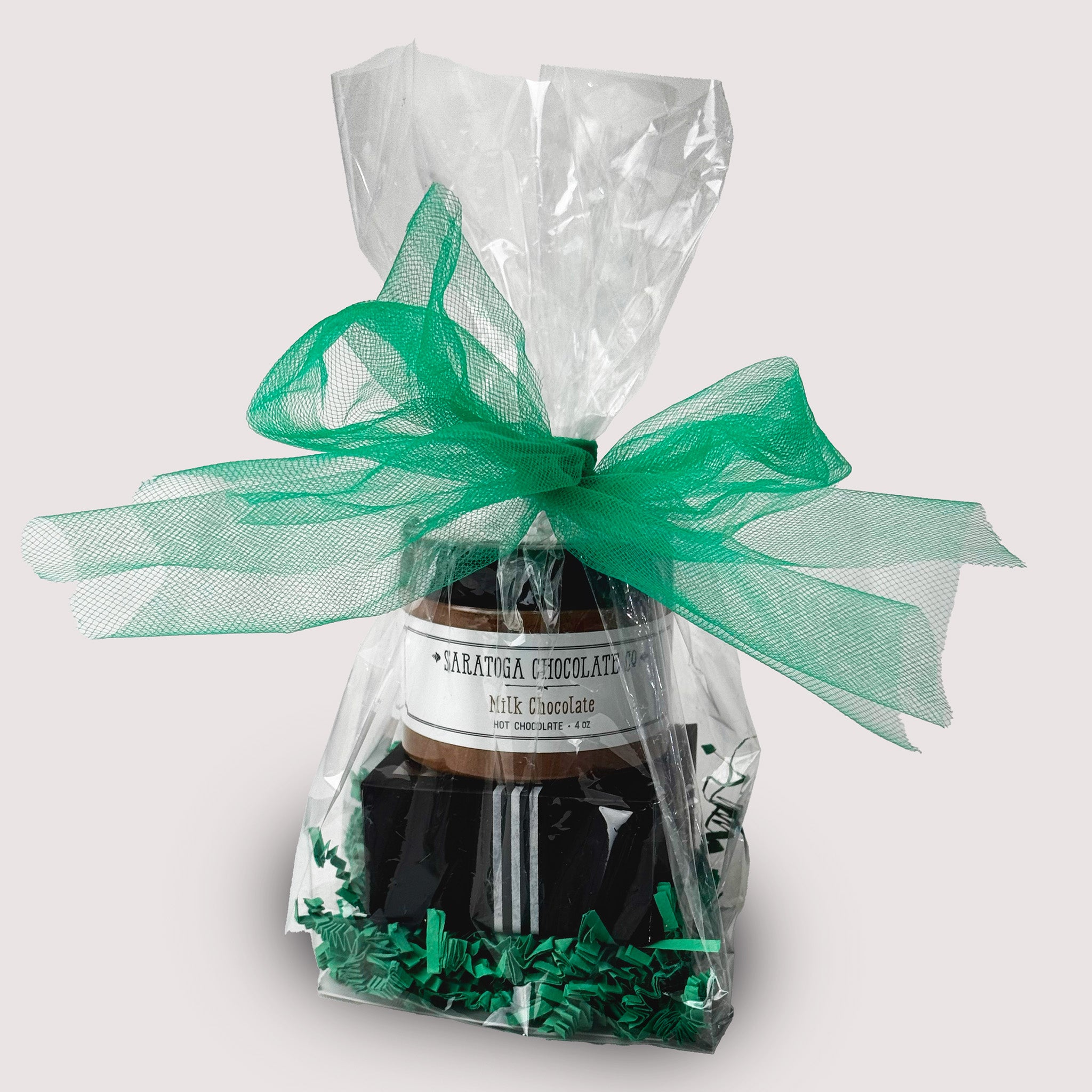A small Saratoga Chocolate Co. St. Patrick’s Day chocolate bundle includes two handmade Irish Cream and two Irish Coffee truffles paired with a small jar of milk chocolate hot chocolate mix  In a clear bag with green ribbon on top.