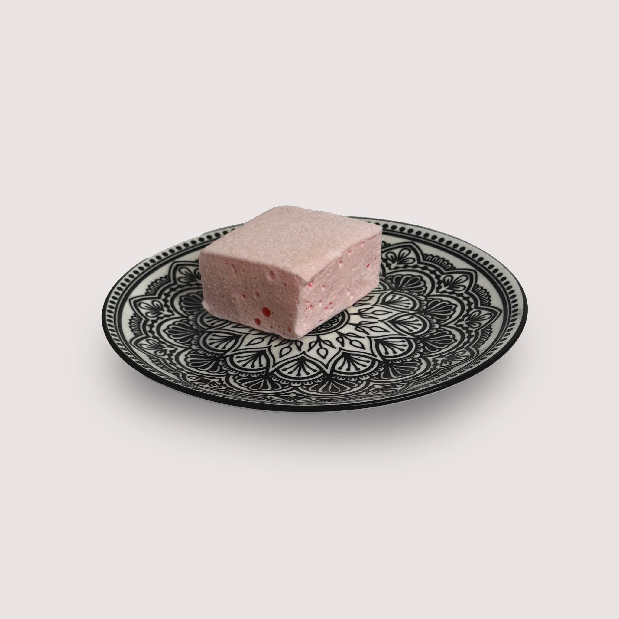 One piece of a jumbo raspberry marshmallow on a plate with black and white pattern.