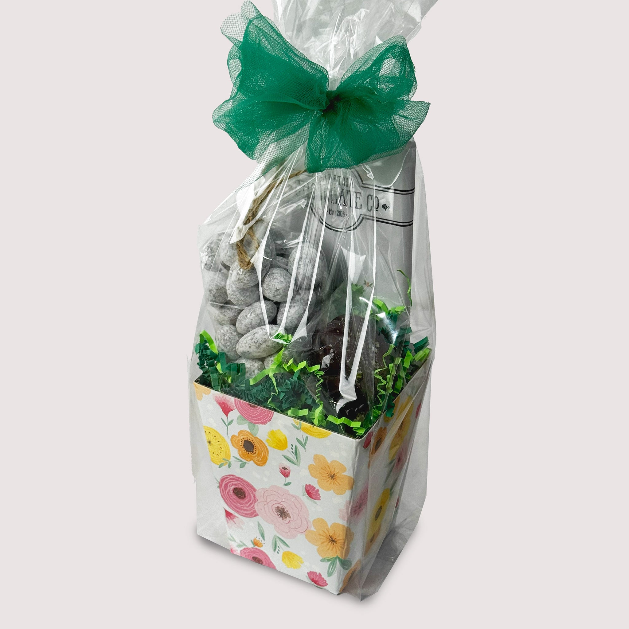 Gift bag with floral design, a Chocolate bar, powdered toffee almonds, and chocolate dipped Oreo in a clear bag on a light gray background