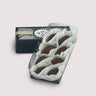 A black box with a clear top of eight Pumpkin Spice Caramel Truffles displayed on a neutral background. Smooth milk and dark chocolate truffles filled with pumpkin caramel, elegantly arranged in white paper cups