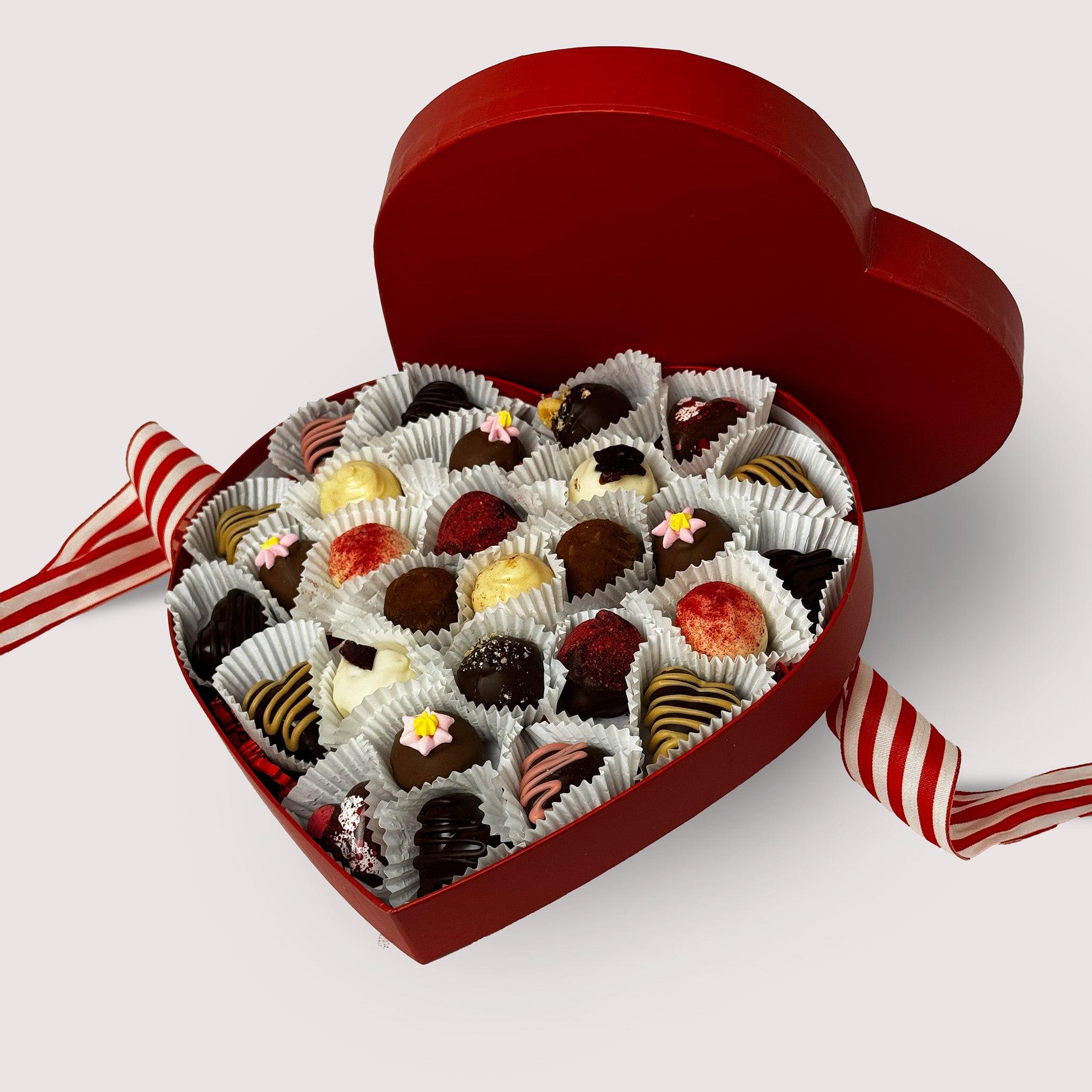 Heart-shaped box of chocolates with a red lid and white interior on a light gray background.