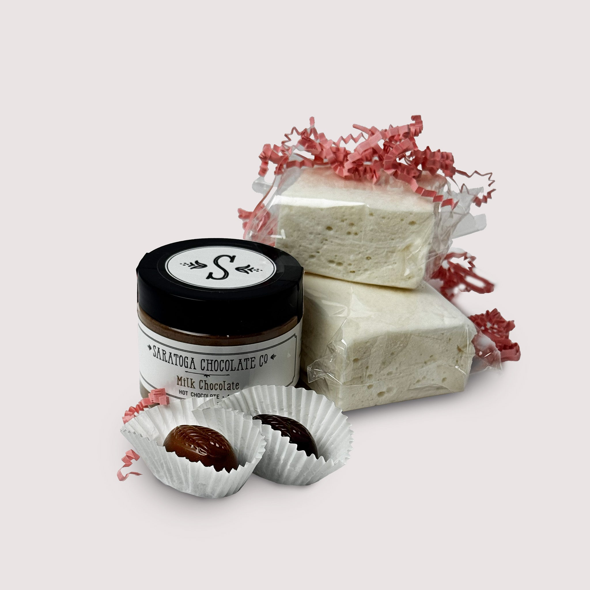 Jar of milk hot chocolate, two pieces of vanilla marshmallow, and a two chocolate truffles on a light gray background.