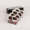 Clear gift box of eight Saratoga Chocolate Co. dark chocolate pinecone-shaped praline bonbons, each nestled in white candy cups on colorful paper crinkle grass. The box features a clear lid with an elegant black border, showcasing the artisanal chocolate presentation. This product contains nuts.