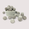 Image shows a pile of powdered sugar coated chocolate coconut flavored toffee macadamia nuts displayed in a fluted white bowl with some powdered sugar coated chocolate coconut flavored toffee macadamia nuts scattered in front 