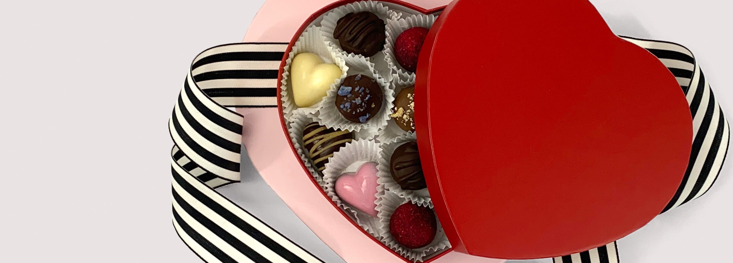 Various chocolate truffles in a red, heart-shaped box with black and white ribbon