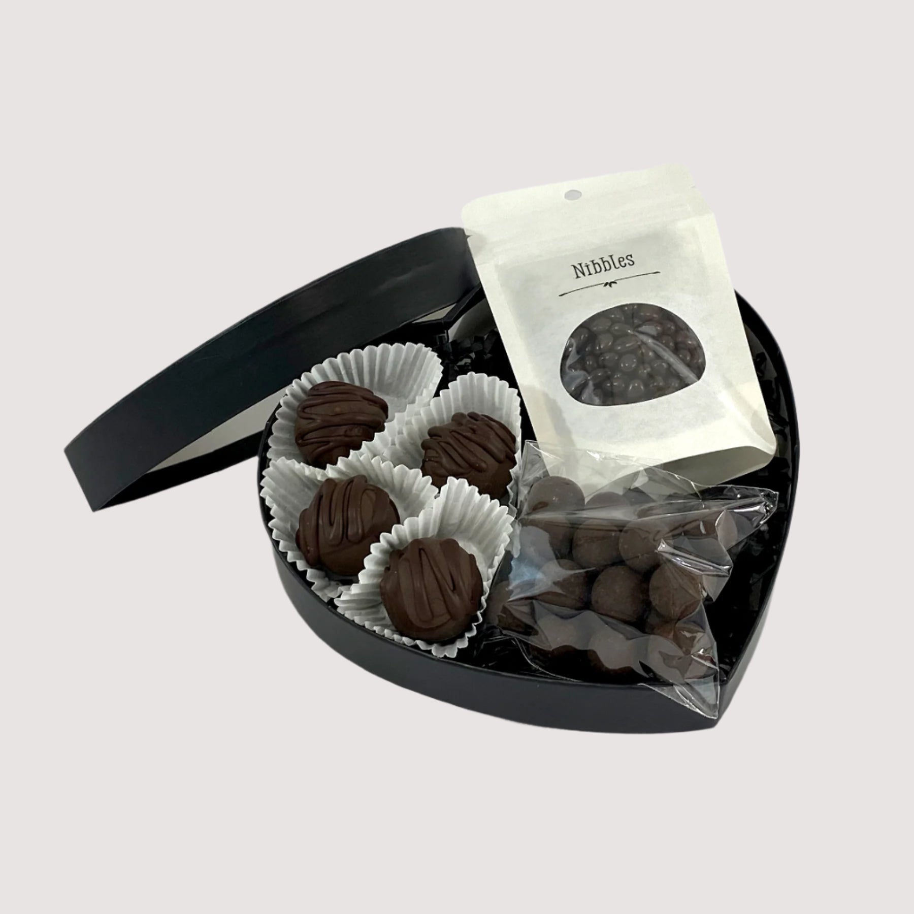 Assortment of truffles, chocolate nibbles, and nuts dipped in dark chocolate, elegantly arranged in a black heart-shaped box.