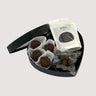 Assortment of truffles, chocolate nibbles, and nuts dipped in dark chocolate, elegantly arranged in a black heart-shaped box.