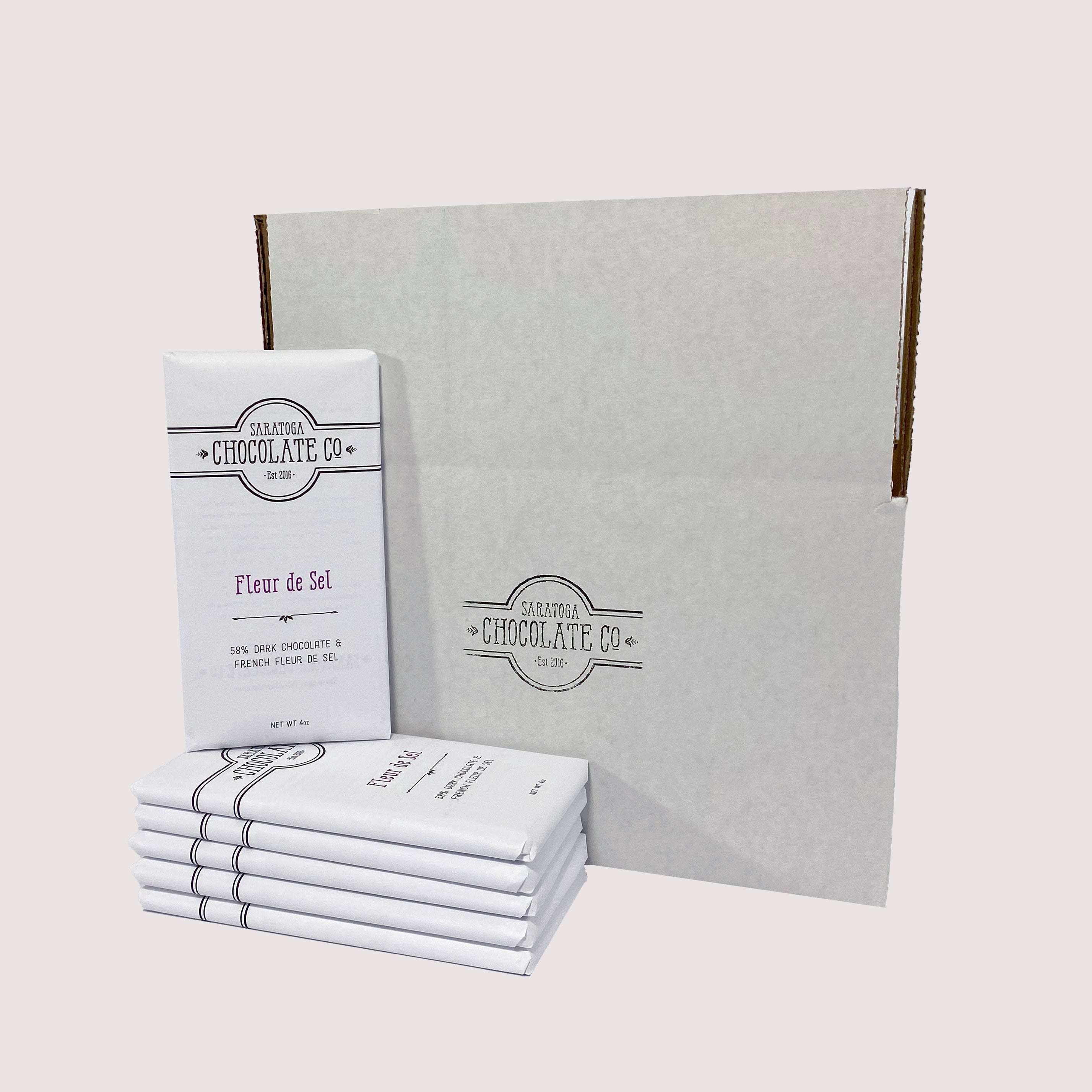 Stack of Saratoga Chocolate Co. bars arranged in front of a white box, with a Fleur de Sel Chocolate bar facing forward and prominently displayed.