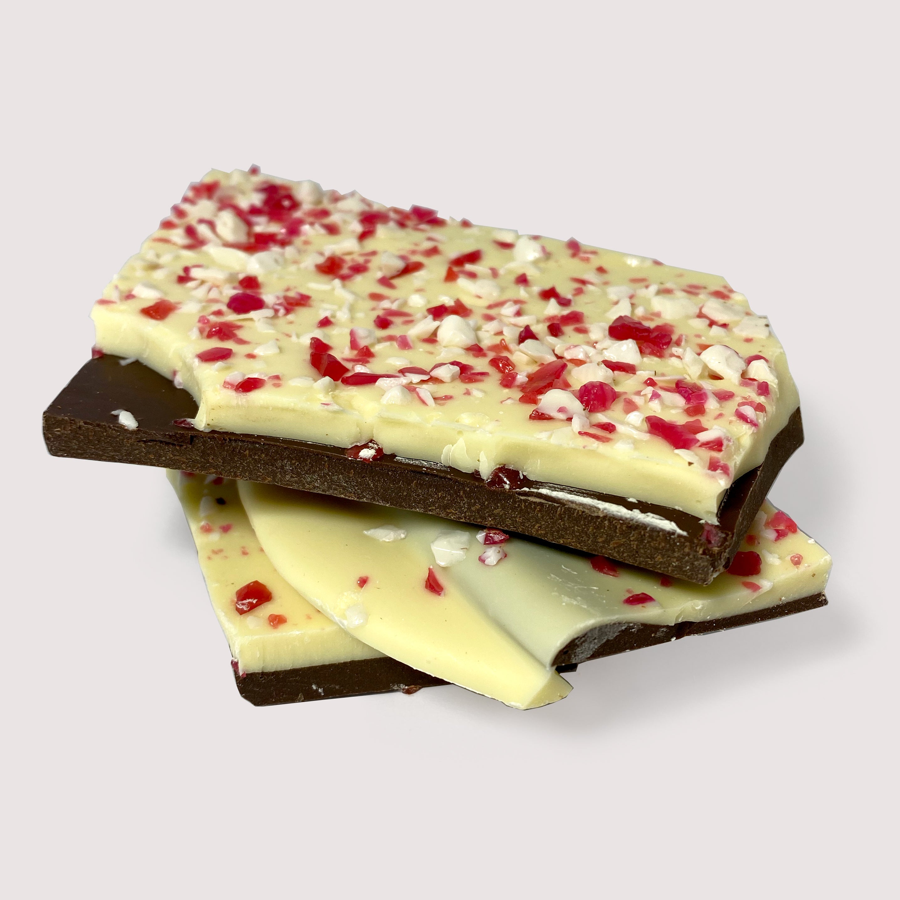 Pieces of dark chocolate bark with crushed peppermint candy on top, stacked on a neutral surface.