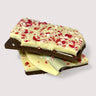 Pieces of dark chocolate bark with crushed peppermint candy on top, stacked on a neutral surface.