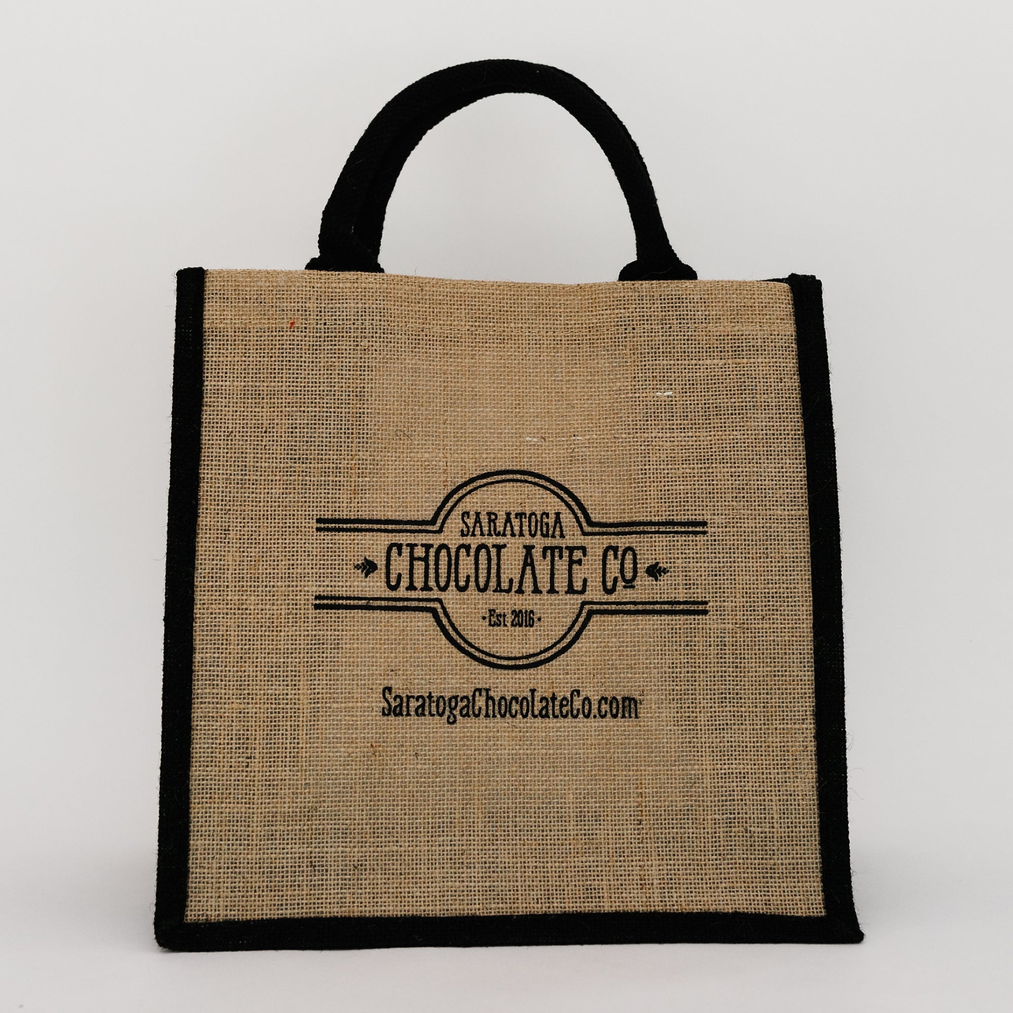 A 12 inch wide by 18 inch tall by 6 inch deep burlap bag with black handles and edging with the Saratoga Chocolate Co. logo embossed on the front of the bag.