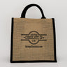 A 12 inch wide by 18 inch tall by 6 inch deep burlap bag with black handles and edging with the Saratoga Chocolate Co. logo embossed on the front of the bag.